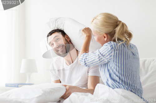 Image of happy couple having pillow fight in bed at home