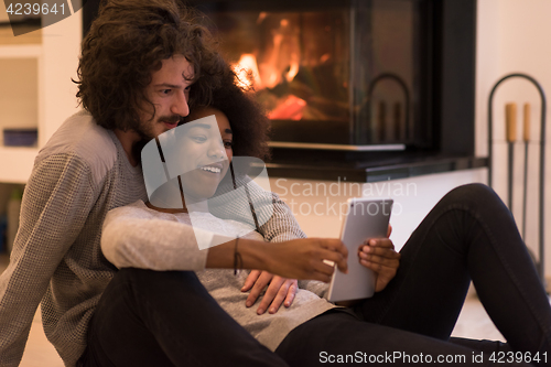 Image of multiethnic couple using tablet computer on the floor