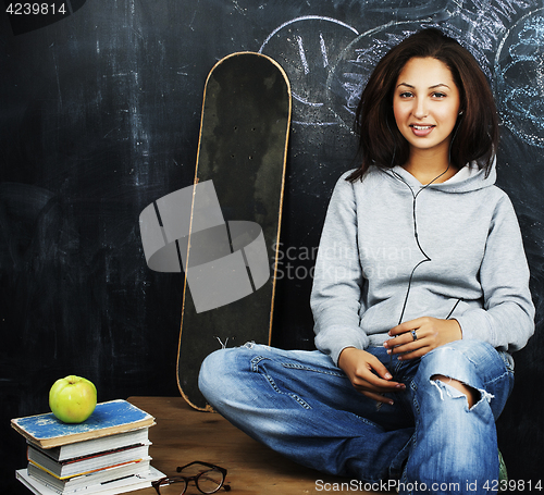 Image of young cute teenage girl in classroom at blackboard seating on ta