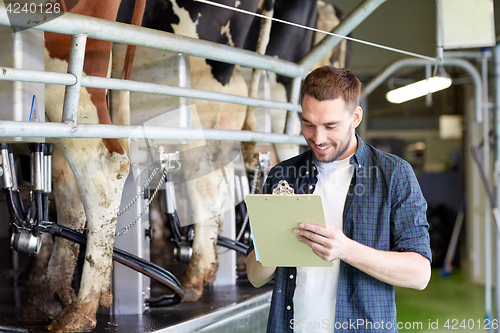 Image of man with clipboard and milking cows on dairy farm