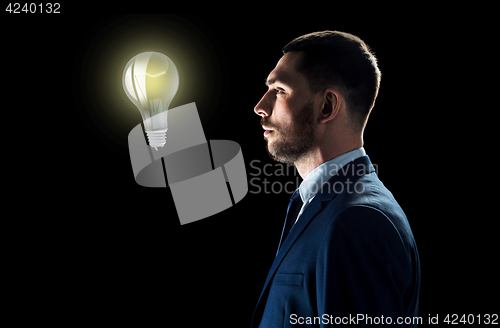 Image of businessman looking at lightbulb over black