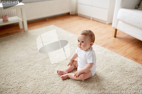 Image of happy baby boy or girl sitting on floor at home