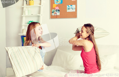 Image of happy teen girl friends fighting pillows at home