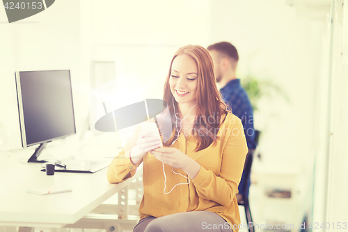 Image of woman with earphones and smartphone at office