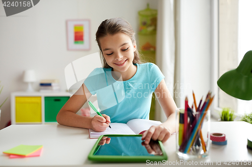 Image of girl with tablet pc writing to notebook at home