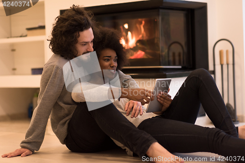 Image of multiethnic couple using tablet computer on the floor