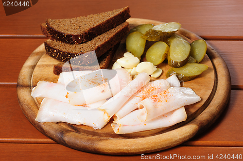 Image of Wooden plate with smoked bacon, pickles and rye bread