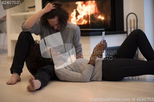 Image of multiethnic couple using tablet computer on the floor