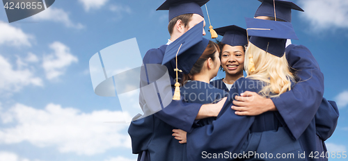 Image of happy students or bachelors hugging over blue sky
