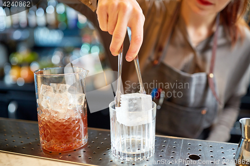 Image of bartender adding ice cube into glass at bar