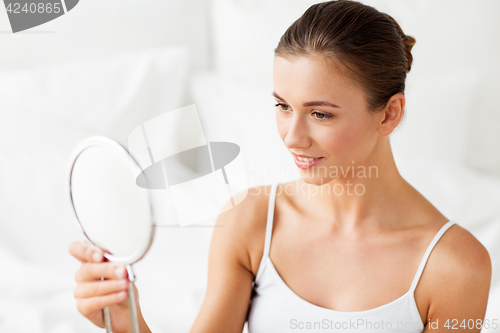 Image of beautiful woman with mirror sitting on bed at home