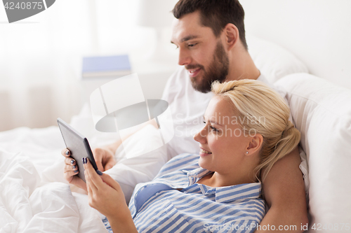 Image of smiling happy couple with tablet pc in bed at home