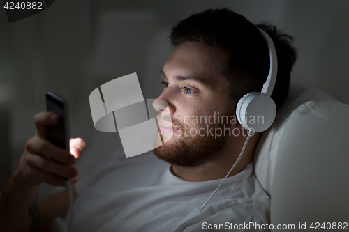 Image of man with smartphone and headphones in bed at night