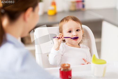 Image of baby girl with spoon eating puree from jar at home