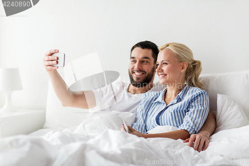 Image of happy couple with smartphone taking selfie at home