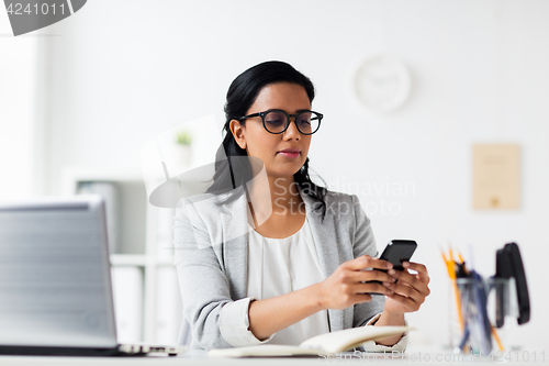 Image of businesswoman with smartphone and laptop at office