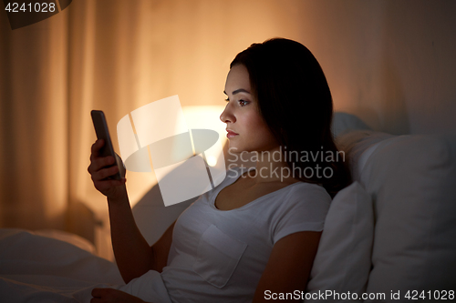 Image of young woman with smartphone in bed at night