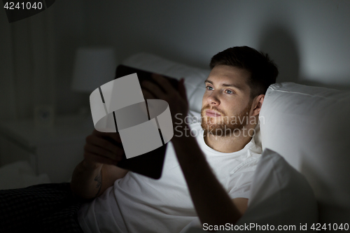 Image of young man with tablet pc in bed at home bedroom