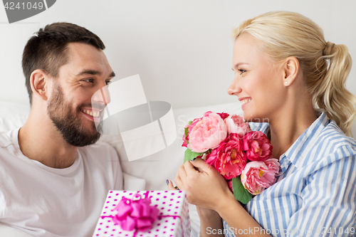 Image of happy couple with gift box in bed at home
