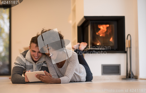 Image of multiethnic couple using tablet computer on the floor