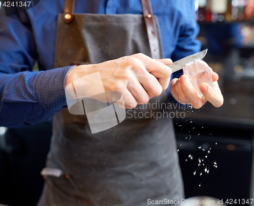 Image of bartender grinding ice cube with knife at bar