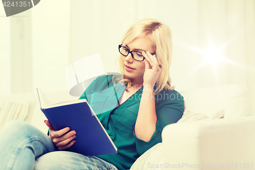 Image of young woman in glasses reading book at home