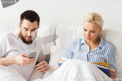 Image of couple with book and smartphones in bed at home