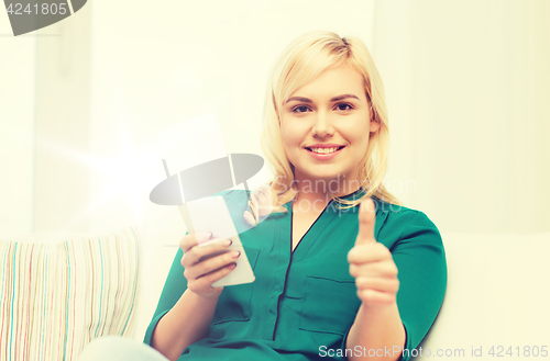 Image of woman with smartphone showing thumbs up at home