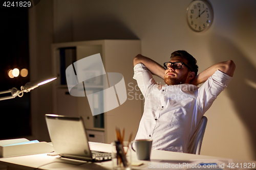 Image of man with laptop stretching at night office