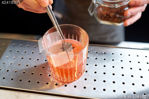 Image of bartender with glass of cocktail and anise at bar