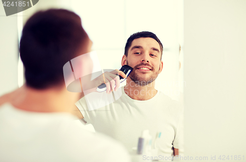 Image of man shaving beard with trimmer at bathroom