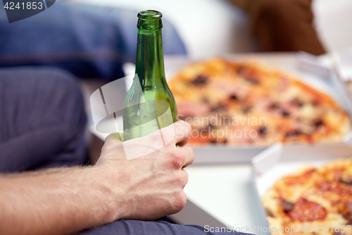 Image of man with beer bottle and pizza at home