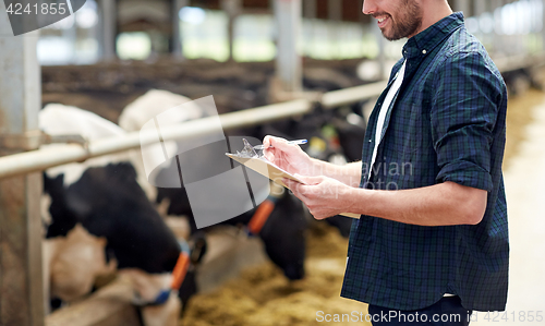 Image of farmer with clipboard and cows in cowshed on farm