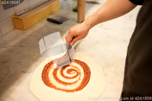 Image of cook applying tomato sauce to pizza at pizzeria