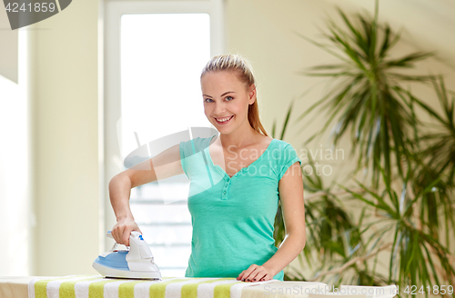 Image of happy woman with iron and ironing board at home