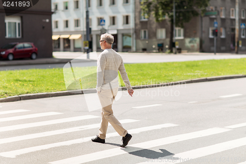 Image of senior man walking along city crosswalk