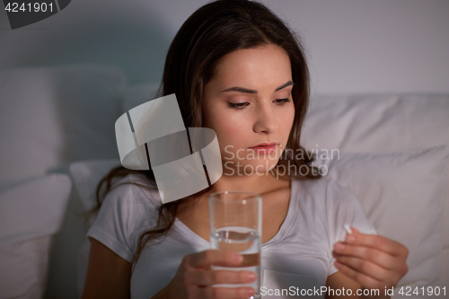 Image of woman with pill and glass of water in bed at home