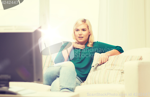 Image of smiling woman with remote watching tv at home