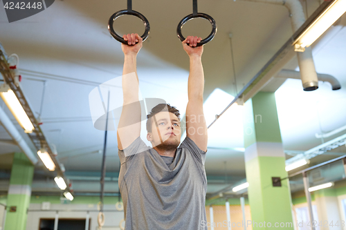 Image of man exercising and doing ring pull-ups in gym