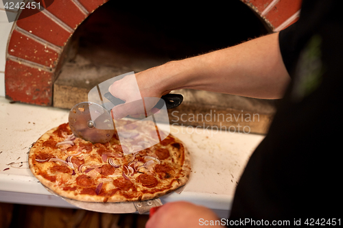 Image of cook hands cutting pizza to pieces at pizzeria