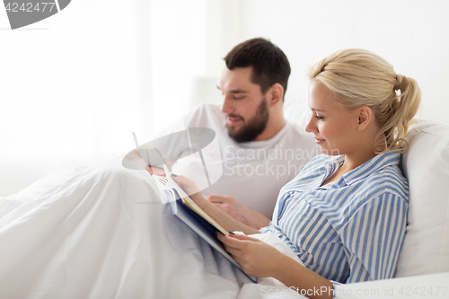Image of couple with book and smartphone in bed at home