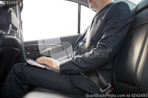 Image of senior businessman with laptop driving in car