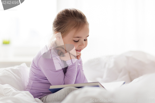 Image of happy little girl reading book in bed at home