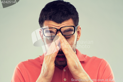 Image of tired man in eyeglasses rubbing eyes