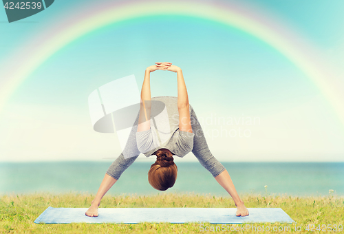Image of woman making yoga wide-legged forward bend on mat
