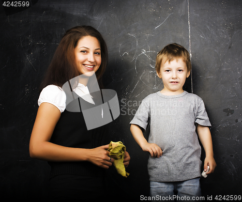 Image of little cute boy with young teacher in classroom studying at blac