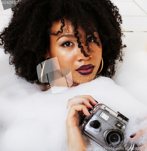 Image of young afro-american teen girl laying in bath with foam, wearing 