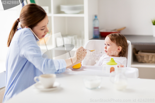 Image of mother with smartphone feeding baby at home