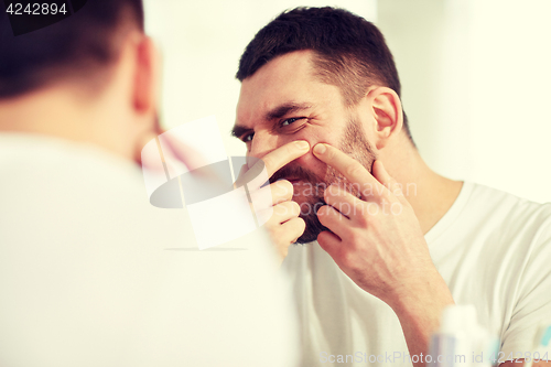 Image of man squeezing pimple at bathroom mirror