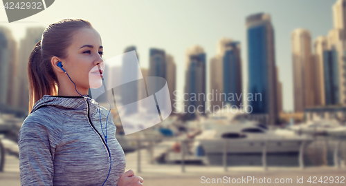 Image of happy woman with earphones running over dubai city